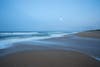 A night shot of a beach with blurred out waves and a bright moon