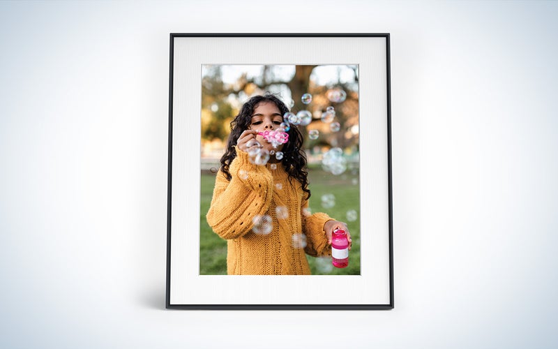 Aura Walden digital picture frame with a photo of a young girl blowing bubbles inside a black frame with a white background.