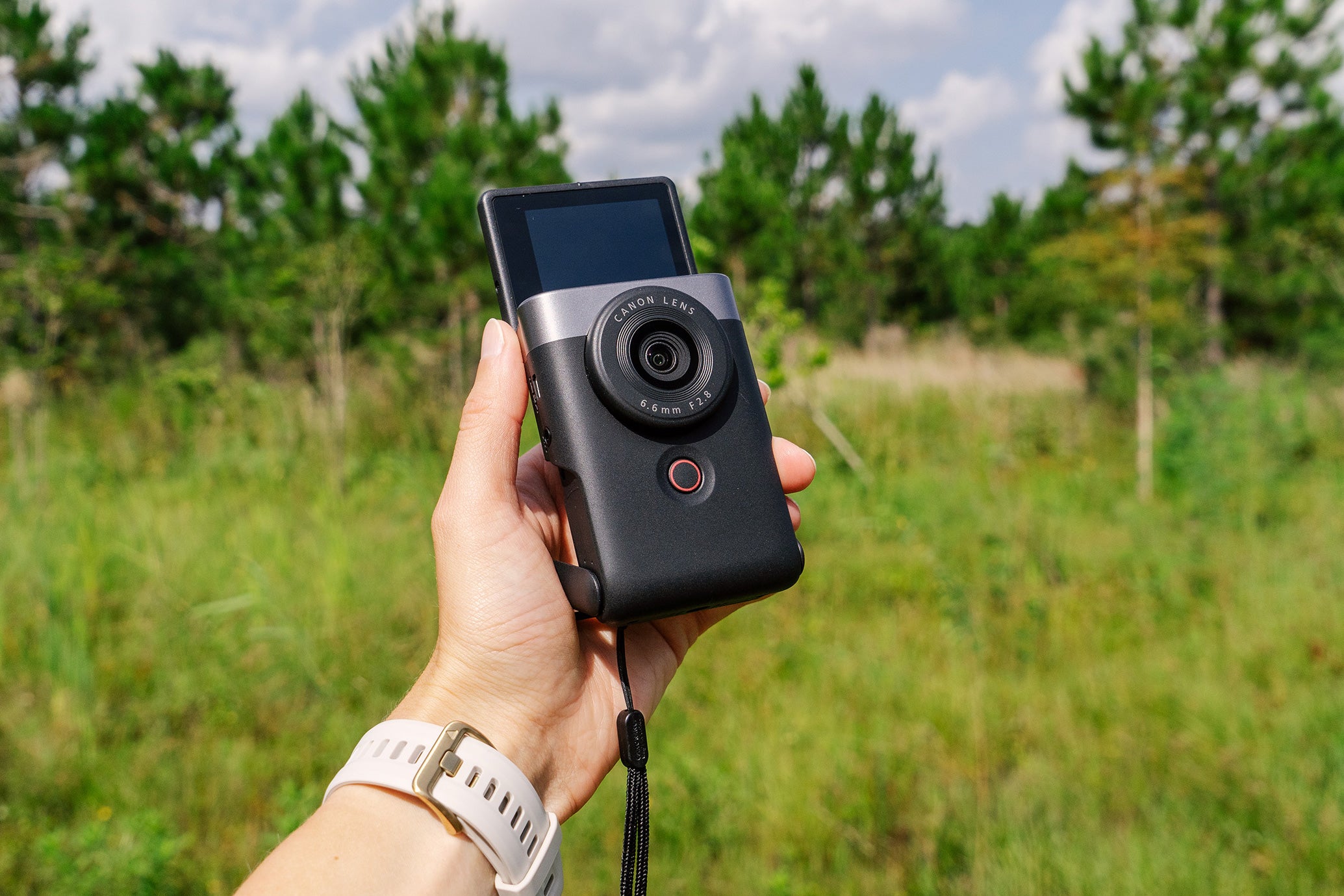 Canon PowerShot V10 vlogging camera in a hand held against a forest background