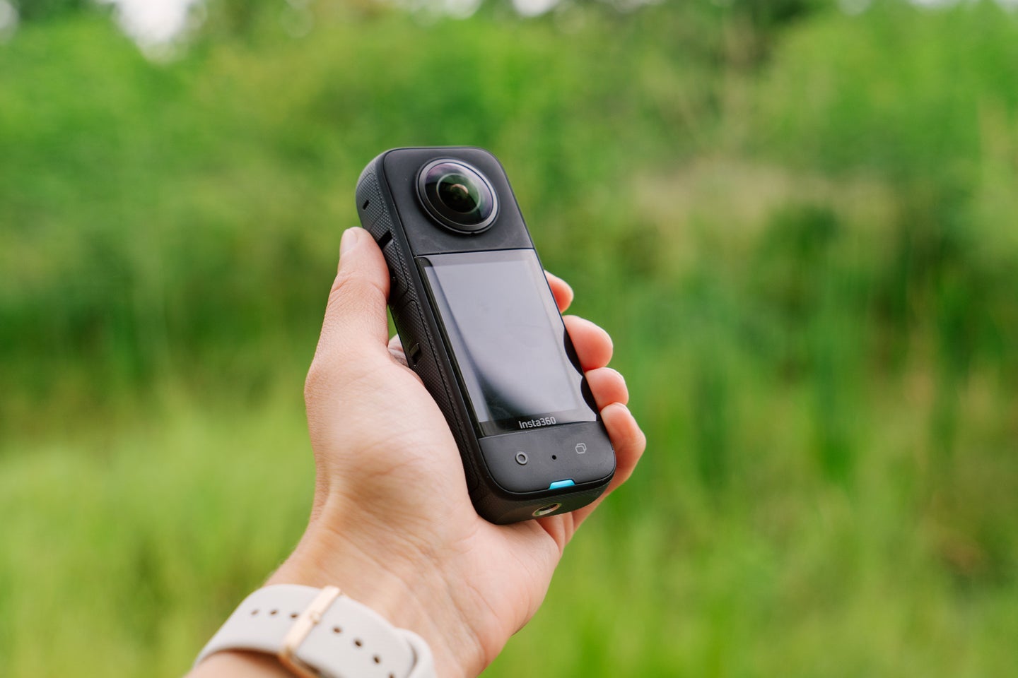The Insta360 X3 in a hand in front of a forest