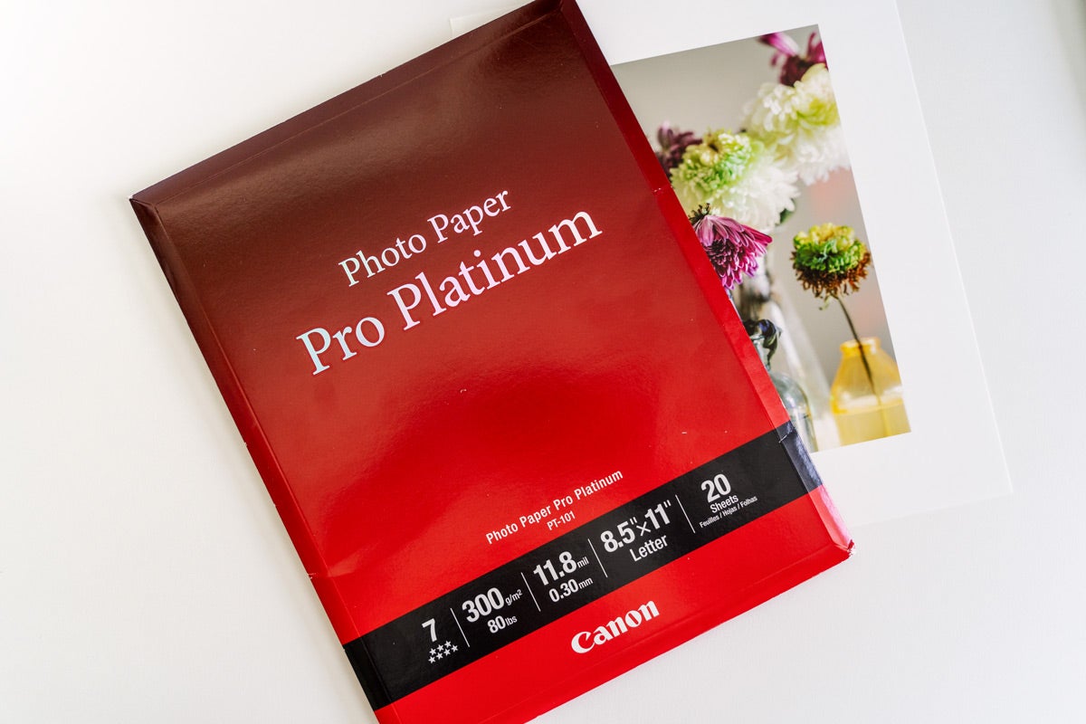 A red package of Canon Pro Platinum photo paper with a printed photograph of flowers underneath rests on a white desk.